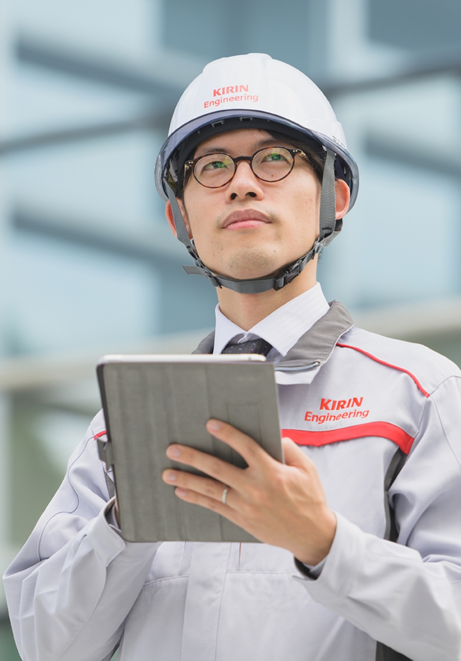 KIRIN Engineeringのヘルメットと作業着を着用し、タブレットを操作している男性社員