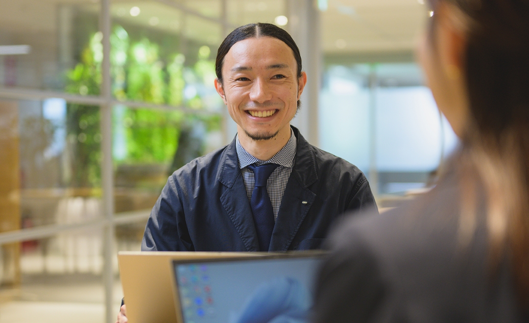 明るいオフィスでノートパソコンを使って笑顔で同僚と会話する社員