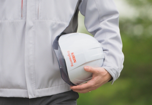ヘルメットを持つ灰色のジャケットを着た男性の姿です。