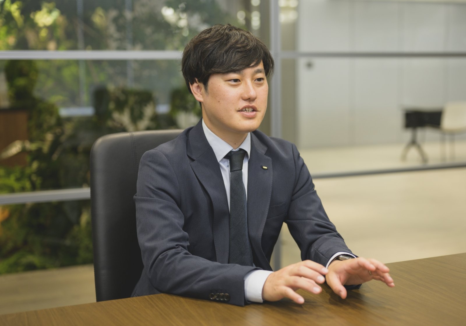 スーツ姿の西沢 和也が社内のオフィスでインタビューに応じている様子