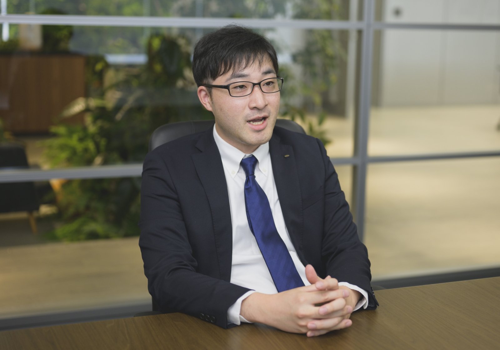 スーツ姿の脇谷 航介が社内のオフィスでインタビューに応じている様子