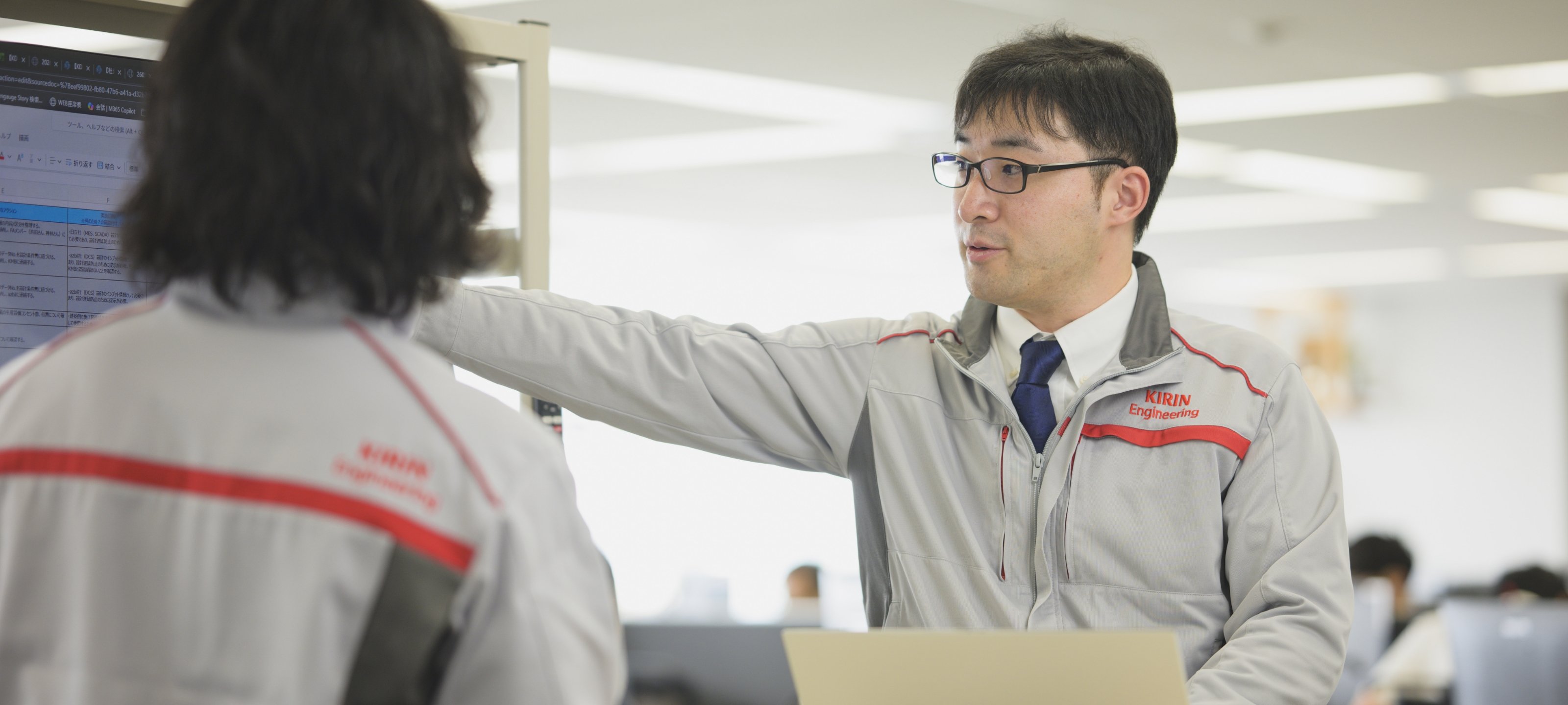 作業服を着て、同僚と画面を確認しながら話す