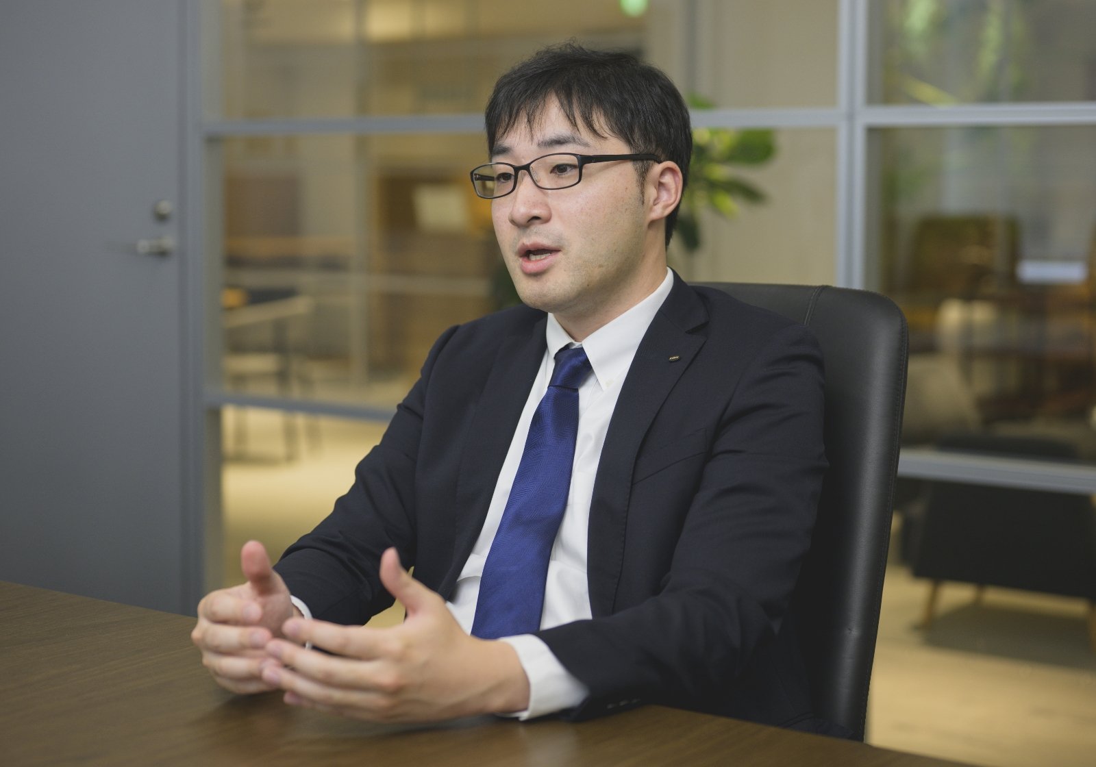 スーツ姿の脇谷 航介がオフィスで真剣にインタビューに答えている様子