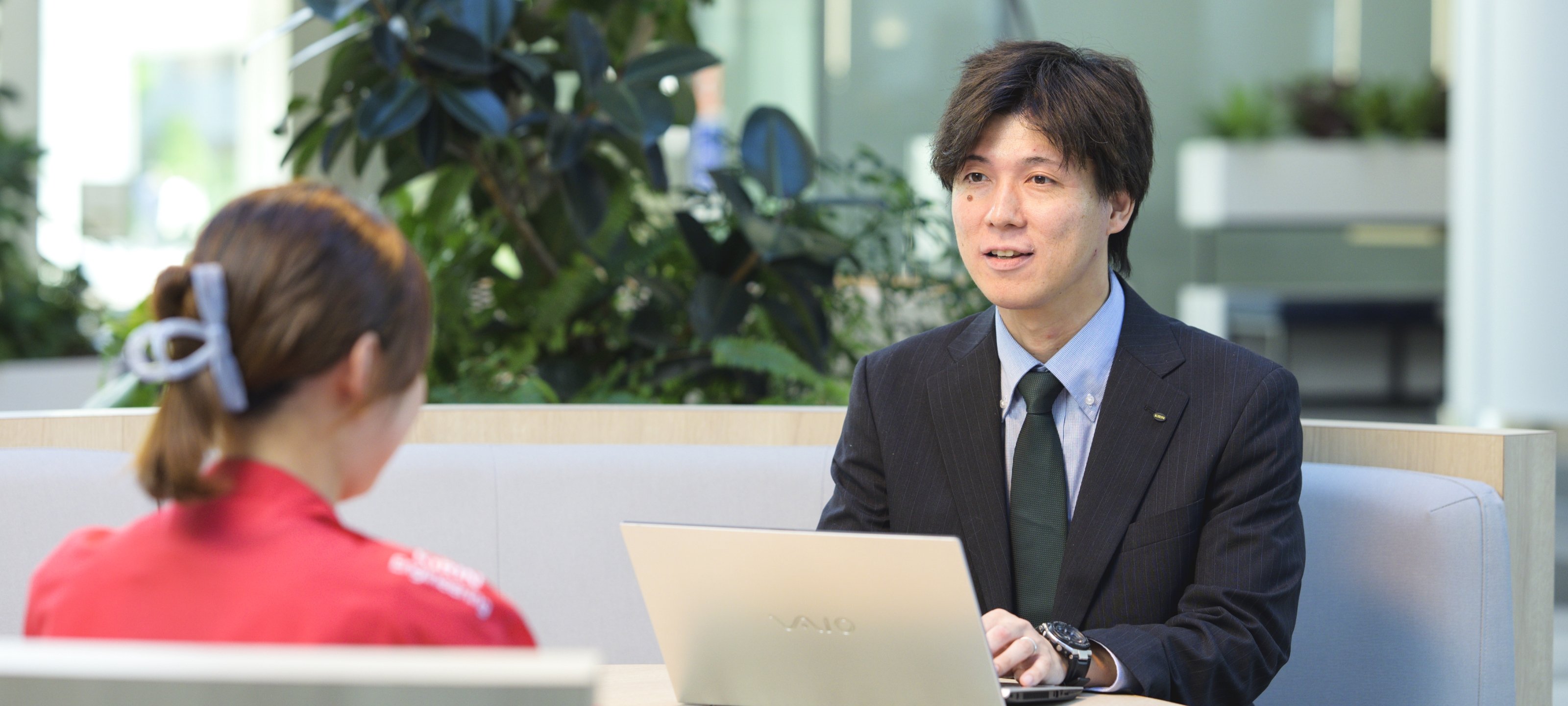 甲斐 正和がオフィスで同僚と笑顔で同僚と談笑している様子