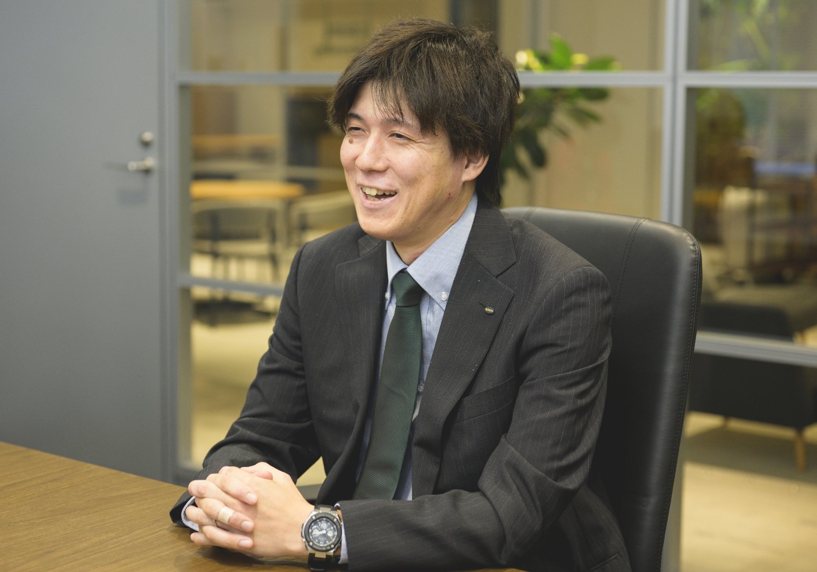 スーツ姿の甲斐 正和がオフィスで真剣にインタビューに答えている様子