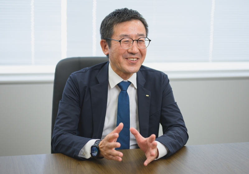スーツ姿の坂本 竜一がオフィスでインタビューを受けている様子