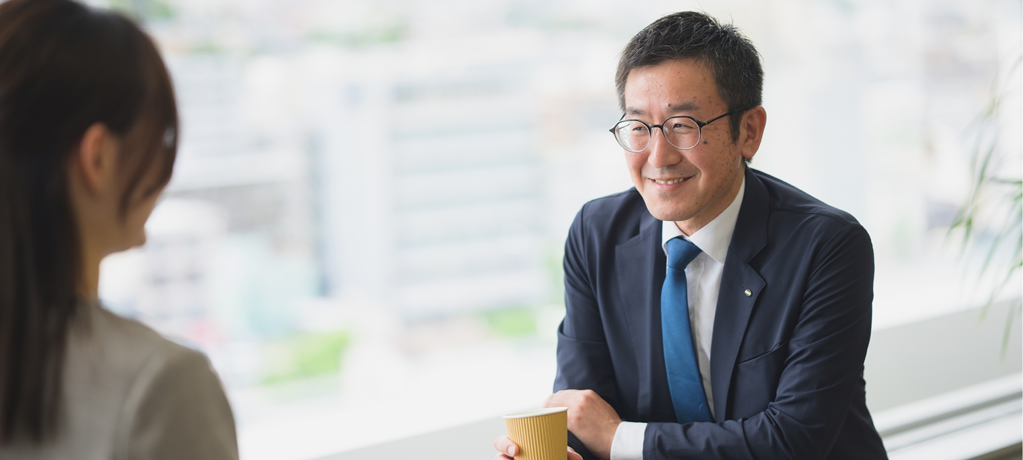 坂本 竜一がオフィスで同僚とコーヒーを飲みながら談笑している様子