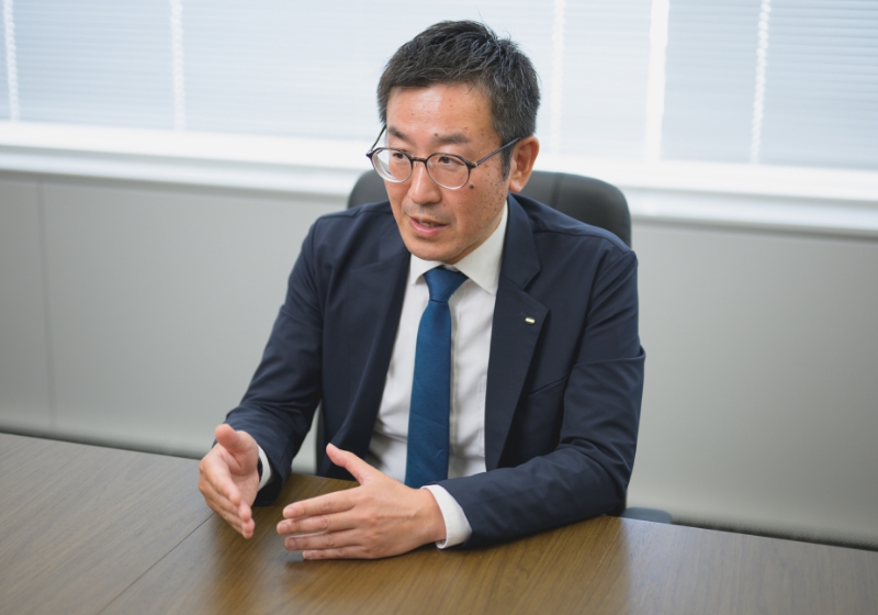 スーツ姿の坂本 竜一がオフィスで真剣にインタビューに答えている様子