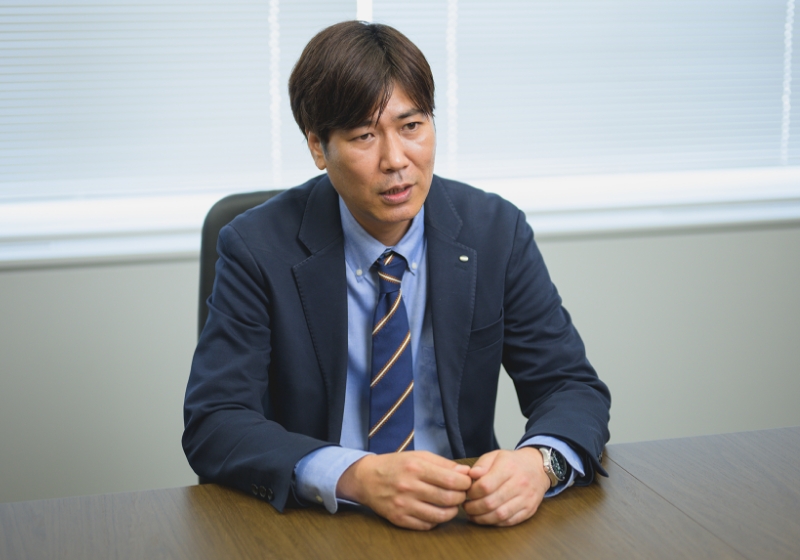スーツ姿の伊藤 崇がオフィスでインタビューに答えている様子