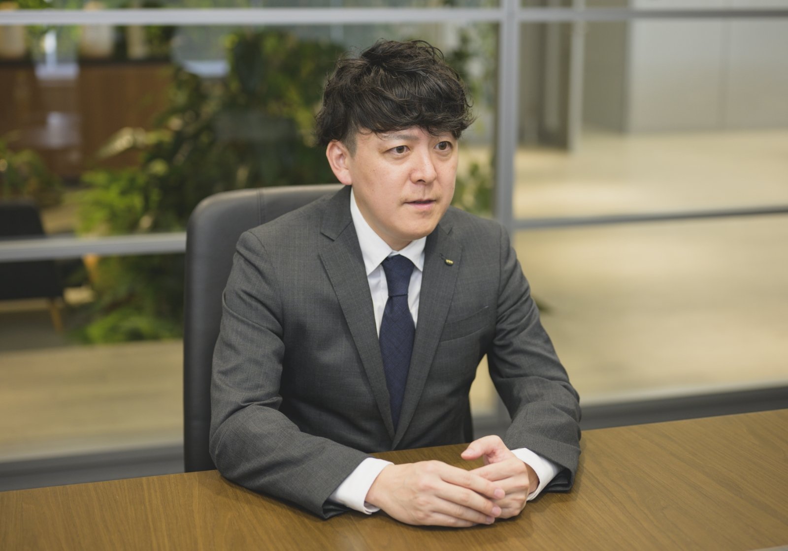 スーツ姿の加藤 雄一が社内のオフィスでインタビューに応じている様子