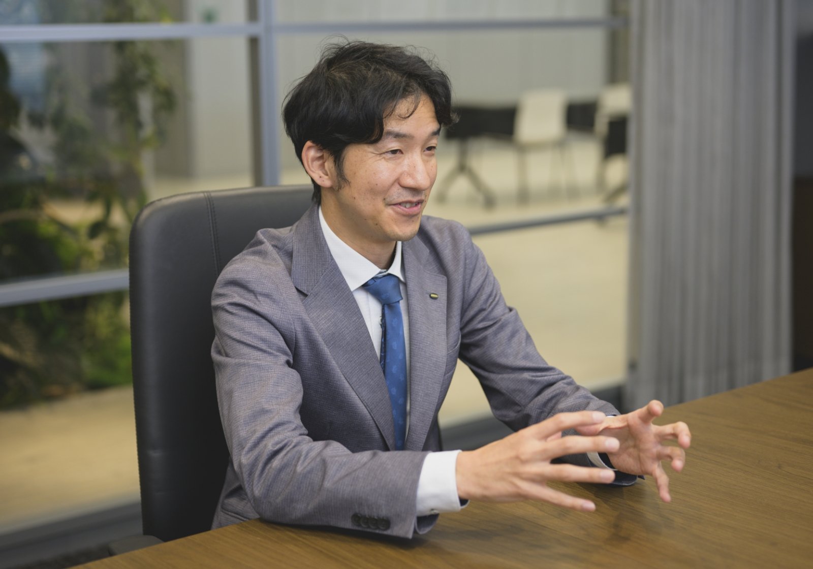 スーツ姿の坂本 優馬が社内のオフィスでインタビューに応じている様子