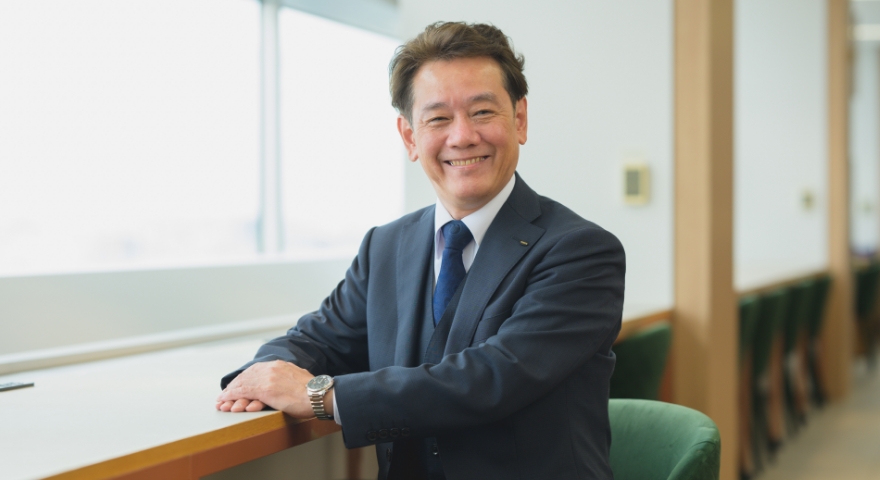 スーツを着た人事総務部長が窓際のカウンター席で笑顔を見せている
