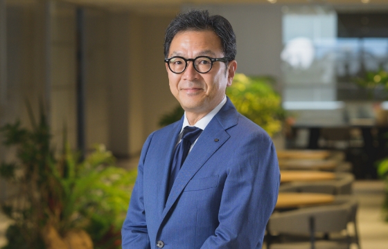 スーツを着た社長がオフィスの観葉植物の前で立っている