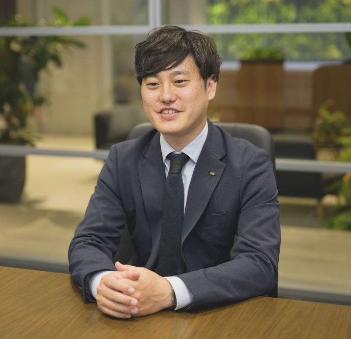 スーツ姿の西沢和也がオフィスでインタビューを受けている様子
