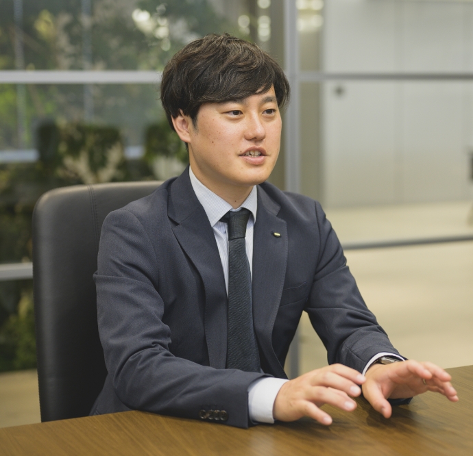 スーツ姿の西沢和也がオフィスでインタビューを受けている様子