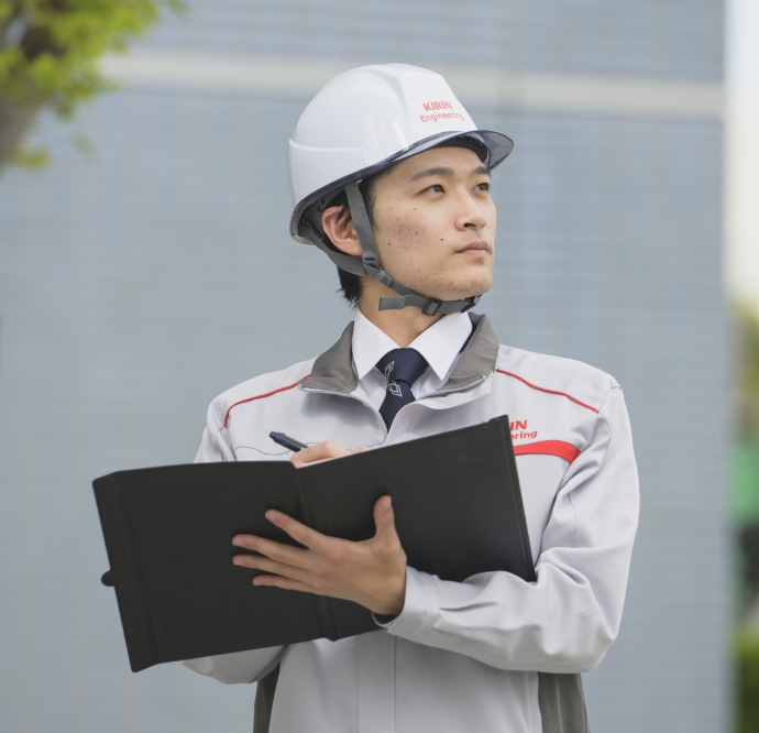 櫻井敬太がヘルメットを着用しバインダーにメモを取りながら真剣な表情で見上げる
