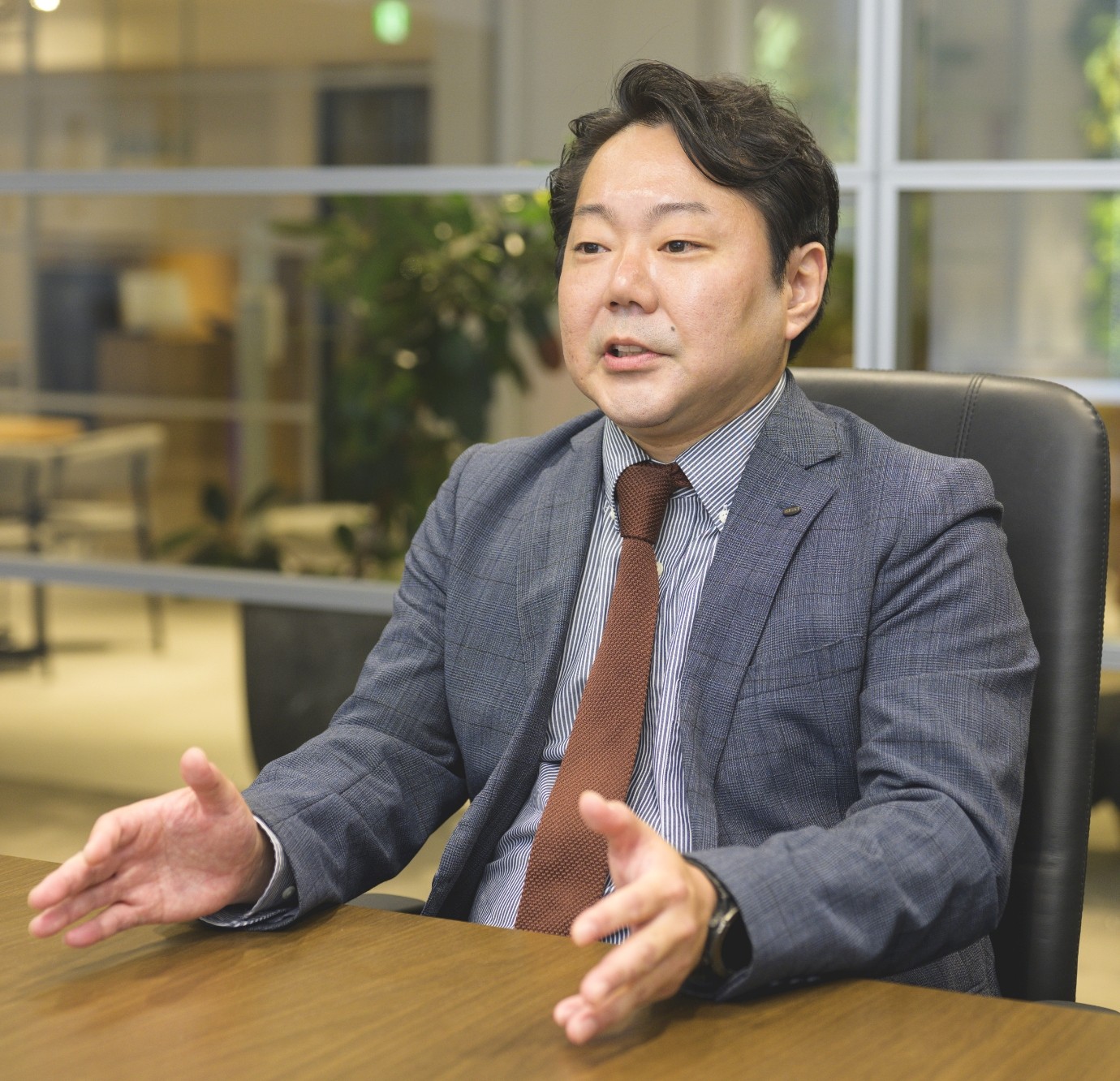 スーツ姿の内田宗正がオフィスでインタビューを受けている様子