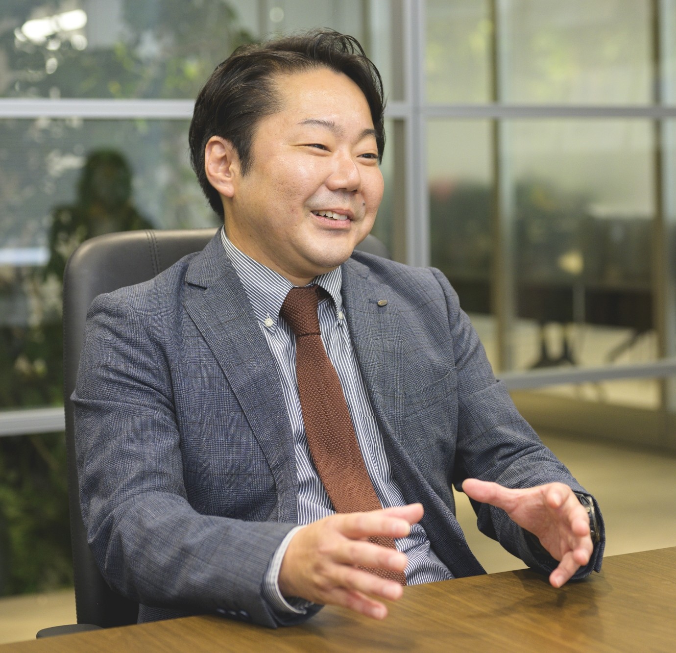 スーツ姿の内田宗正がオフィスでインタビューを受けている様子